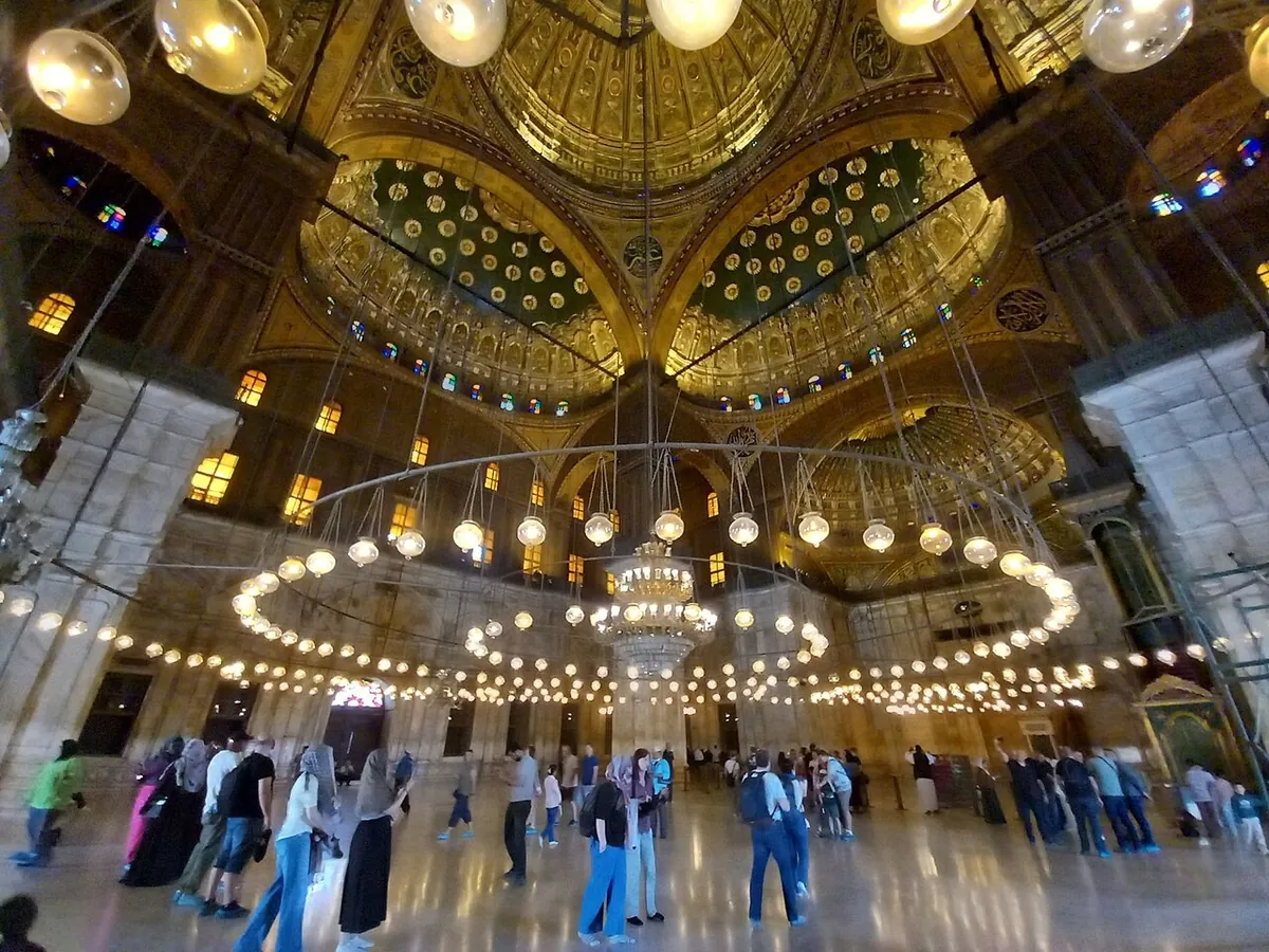 Besucher unter den hängenden Lampen und bemalten Kuppeln in der Muhammad-Ali-Moschee
